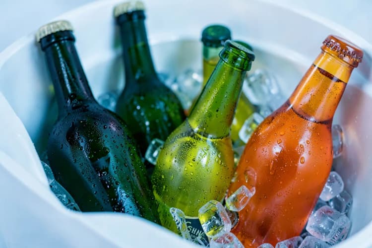 Garrafas de vinho, cerveja e refrigerante em um cooler com gelo.