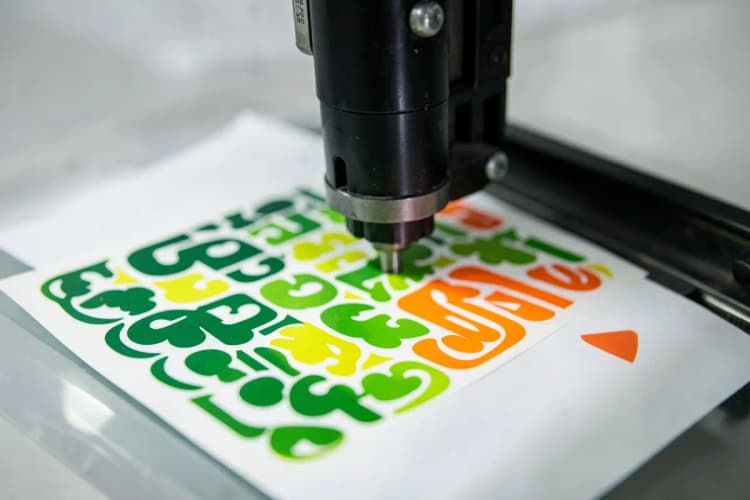Uma máquina de corte de precisão cortando formas complexas em folhas de adesivos personalizados.