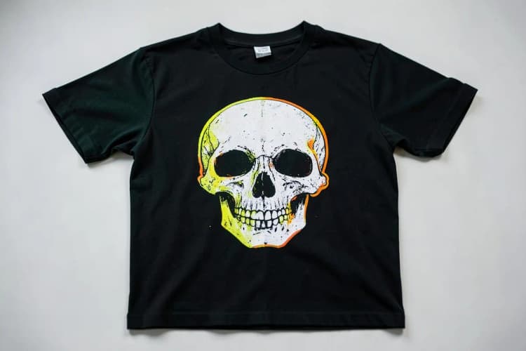 Camiseta preta com estampa de caveira estilizada em branco, vista de cima.
