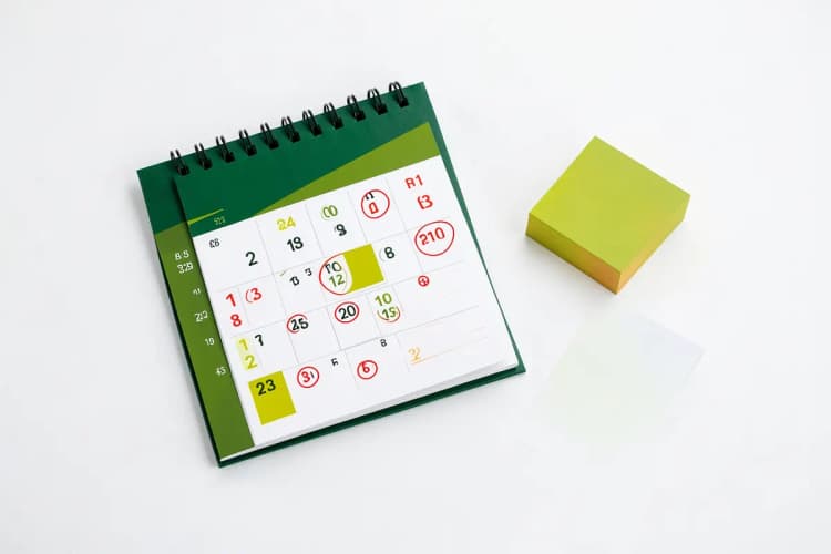 Um calendário de mesa com datas marcadas e um pequeno pacote de cartões de visita ao lado.