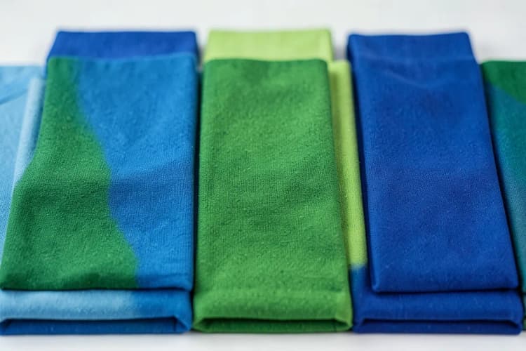 Close-up de amostras de tecido de camisetas coloridas em tons de azul e verde, com texturas variadas.