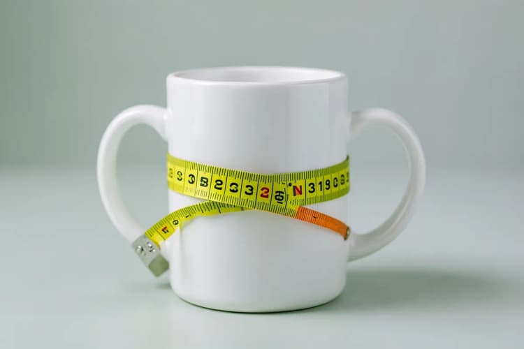 Uma caneca branca com uma fita métrica enrolada em volta.