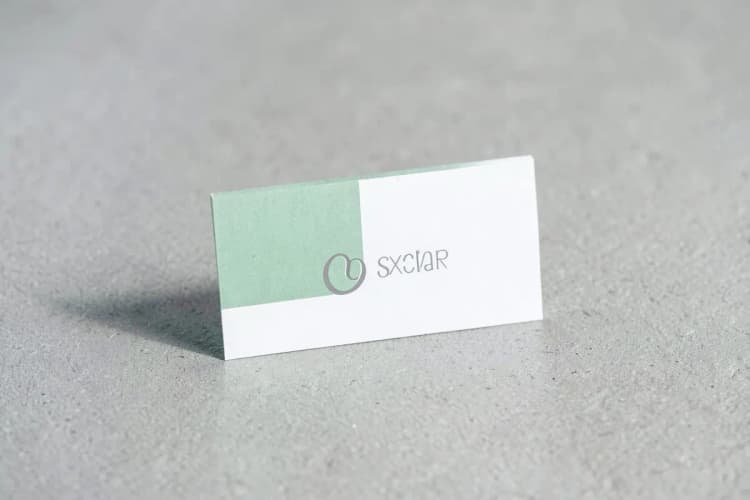 Um cartão de visita com design minimalista e tipografia elegante, em tons de cinza e branco, sobre uma superfície texturizada.
