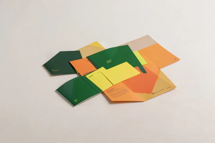 Composição de materiais gráficos impressos, como cartões de visita, flyers e folders, dispostos de forma organizada sobre uma mesa.
