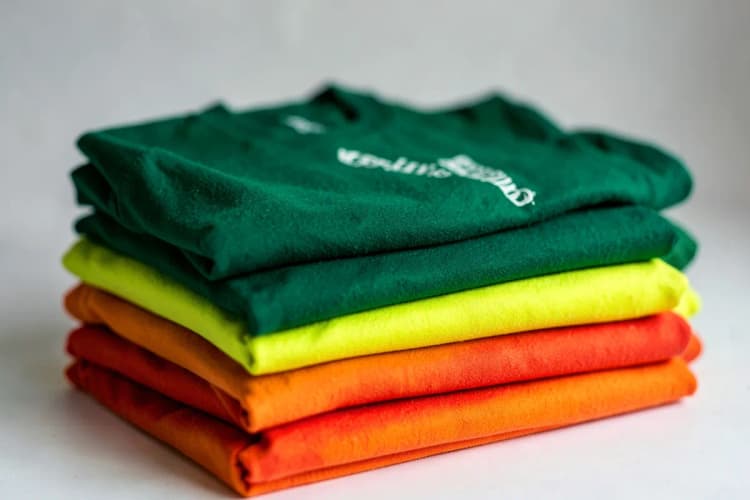 Camisetas promocionais de diferentes cores e tamanhos empilhadas