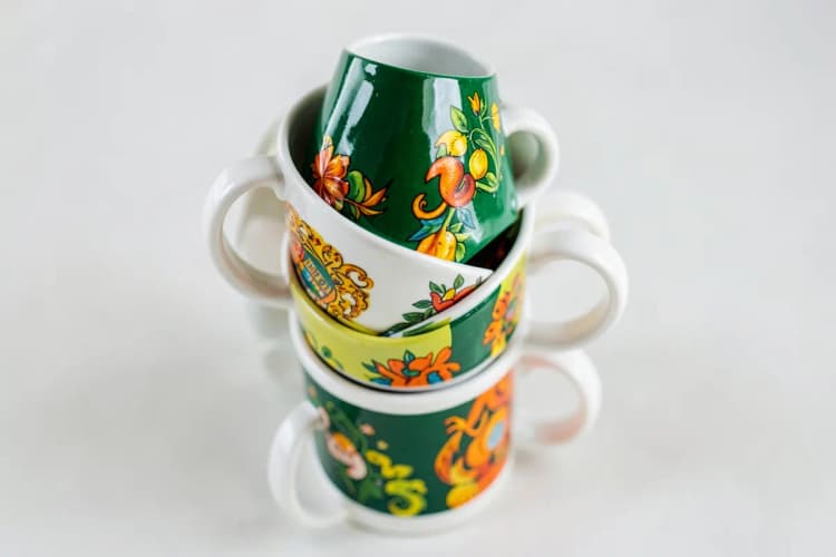 Diversas canecas brancas empilhadas, algumas com estampas coloridas variadas.