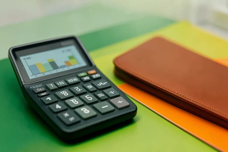 Uma calculadora mostrando números e um gráfico de custos em uma mesa.