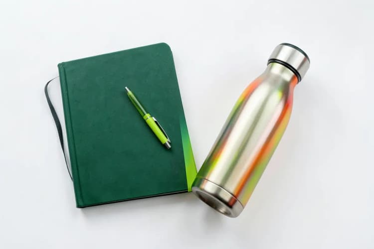 Uma pessoa anotando em um caderno com uma caneta ao lado de um brinde.