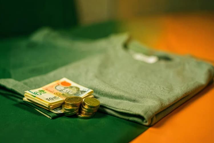 Moedas e notas de dinheiro empilhadas ao lado de uma camiseta dobrada.