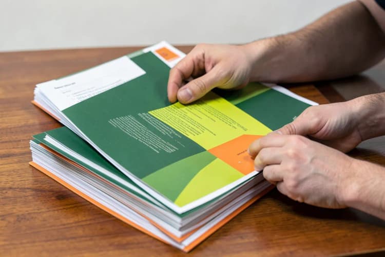 Uma pessoa organizando pilhas de papéis impressos em uma mesa de madeira, com foco em um panfleto aberto.