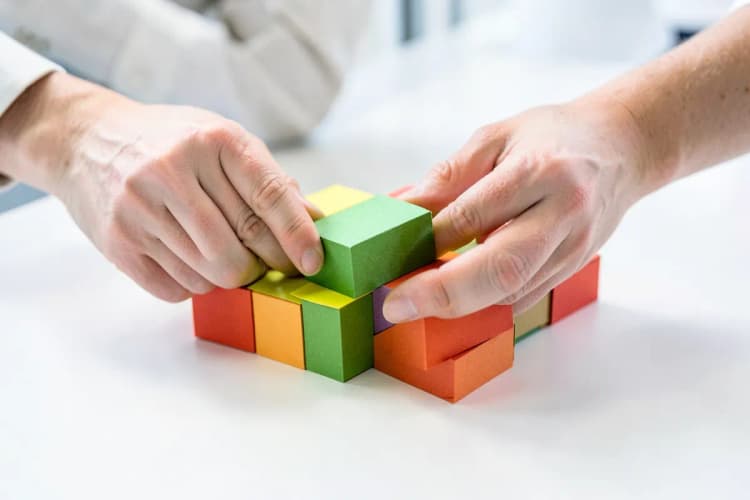 Mãos organizando blocos de papel coloridos em uma mesa.