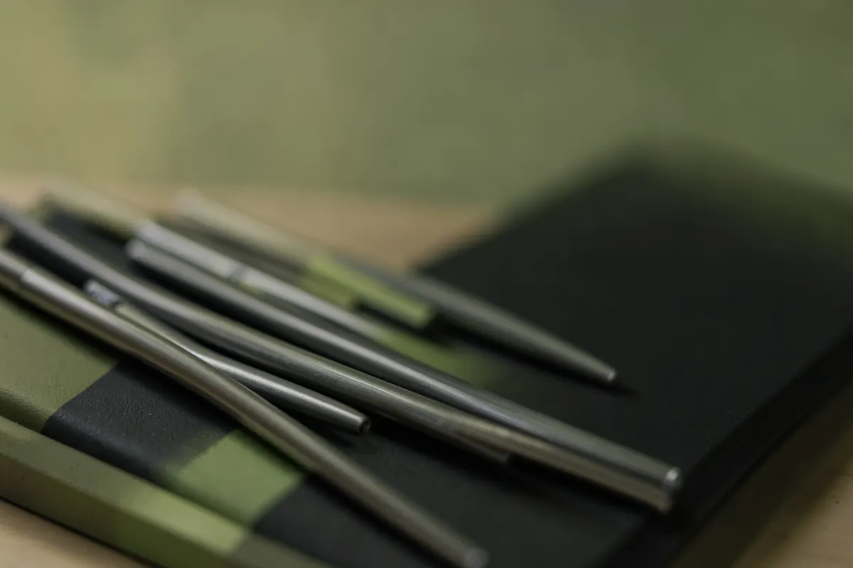 Detalhe de canetas de metal escovado e blocos de notas com capa preta em uma mesa.