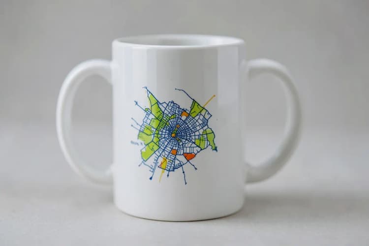 Close-up de uma caneca de cerâmica branca com a frase 'Eu amo Recife' em letras pretas e um desenho do mapa da cidade em azul.